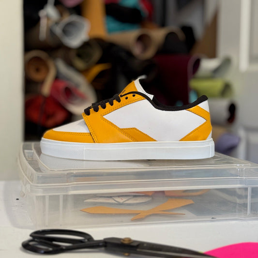 Yellow and white sneaker on a clear shoebox with scissors and colorful items in the background